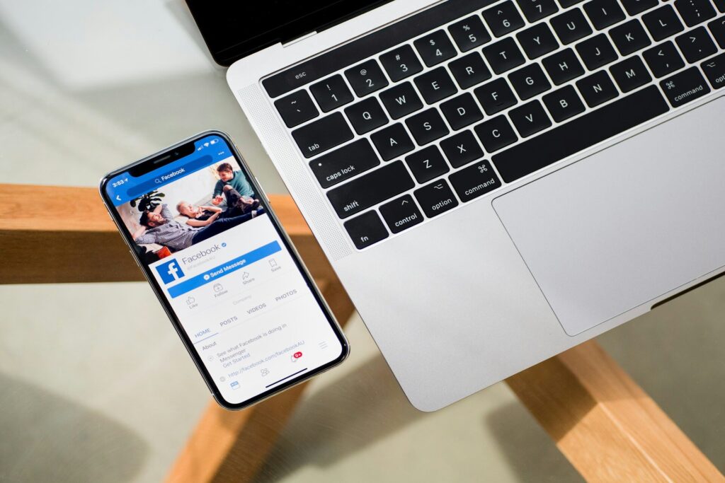 Facebook app on mobile phone next to laptop