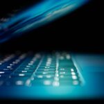 Close-up of a laptop keyboard with blue backlighting and a shallow depth of field, creating a bokeh effect.