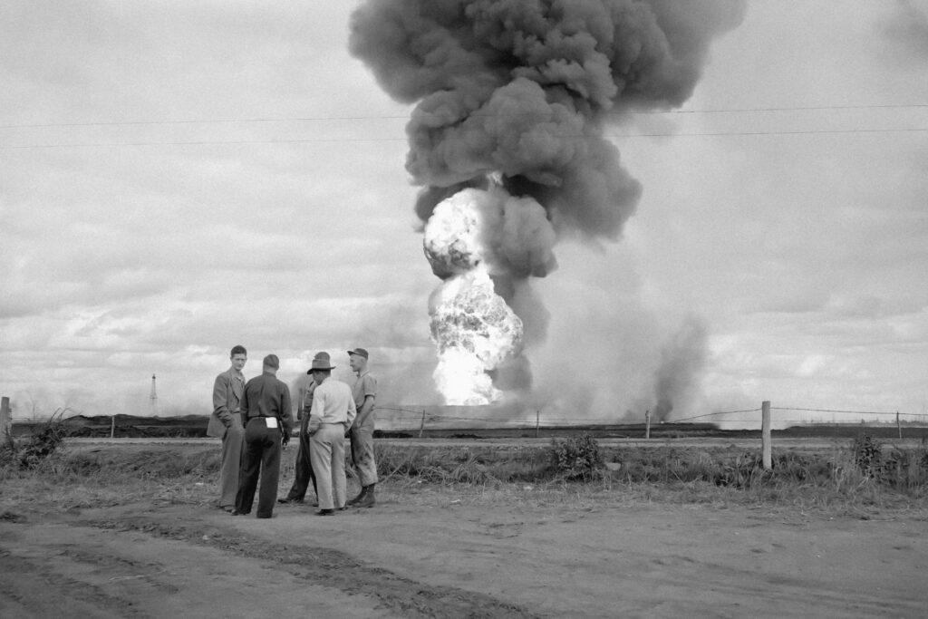 Black and white image showing a group of people observing a massive plume of smoke rising into the sky.