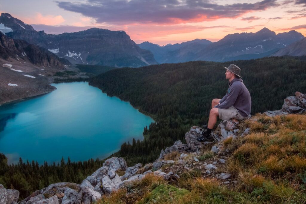 A man relaxes on a mountain peak, enjoying a breathtaking view of a lake below.