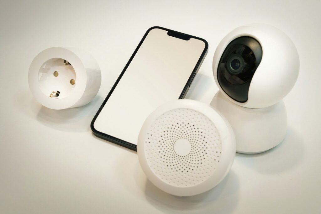 A smart home security camera alongside a smartphone and a speaker