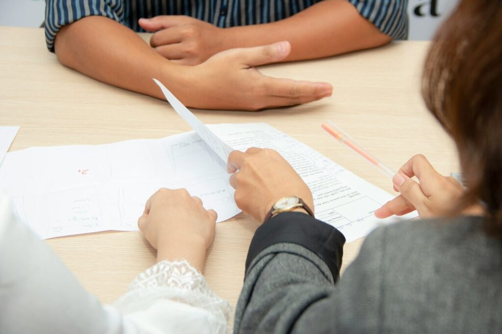 A person being interviewed by two people who are looking through paperwork.
