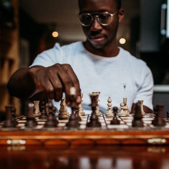 A man sitting at a chessboard, moving a piece.